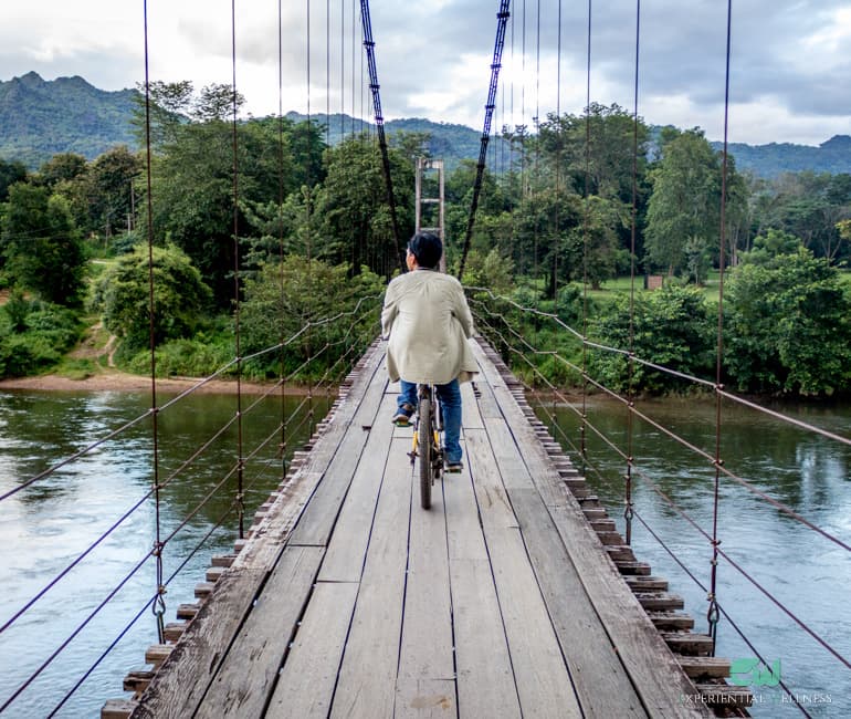 Ein Mann fährt mit dem Fahrrad über die Hängebrücke am River Kwai