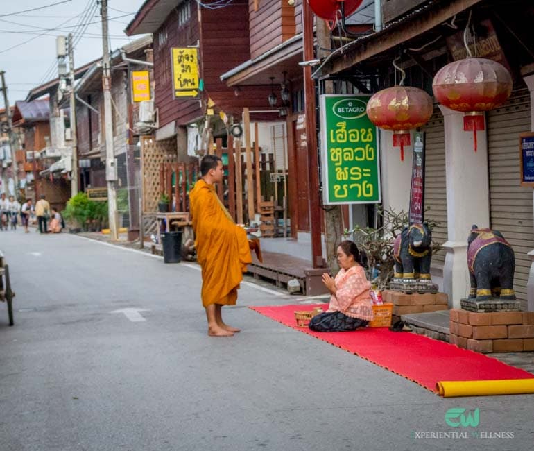 Eine Einheimische übergibt einem buddhistischen Mönch Almosen