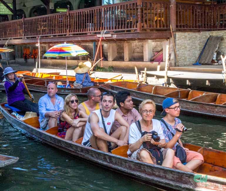 Eine Einheimische rudert ihr traditionelles Boot mit Reisenden durch den schwimmenden Markt Damnoen Saduak