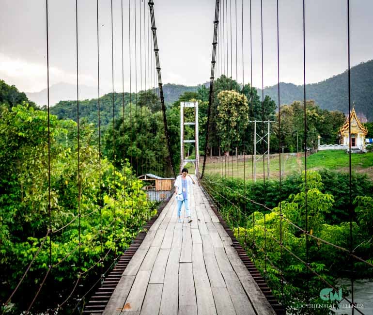 Mädchen überquert eine hölzerne Hängebrücke auf dem Rückweg von einem lokalen thailändischen Tempel